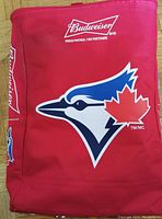 Front side of red cooler bag showing Budweiser and Toronto Blue Jays logos.