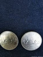 Pair of 1981 Canadian silver dollar coins with Voyageur design showing two men paddling a canoe and northern lights.