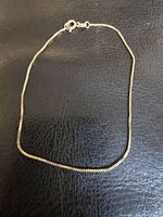 Full view of delicate 10kt gold bicycle link bracelet laid flat on black surface, showing chain links and clasp.