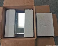 Top down view showing one mirror pedestal enclosed in white foam packaging inside a cardboard box.