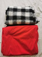 Folded black and white checkered pants on top of folded red sweatpants.