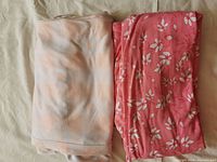 Two folded garments on a light background: one light pink and white checkered pants, and one pink floral patterned fabric garment.