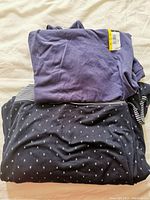 Folded purple top with yellow tag on top of folded striped and patterned tops