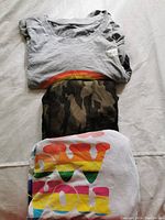 Folded grey tank top with faint visible rainbow and tag visible on shirt, indicating brand new condition.