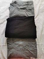 Two gray t-shirts and one pair of black shorts folded neatly on a white background.
