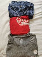Overview of three folded plus size 5XL clothing items: blue plaid button-up shirt, red graphic t-shirt, grey t-shirt.