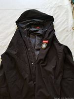 Black plus size raincoat with hood, snap button closure, chest patch and brand script on inner flap