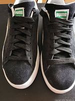 Top front view of pair of black suede Puma casual shoes with white soles and laces tied.
