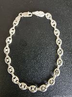 Full view of the silver bracelet laid out on a dark surface showing mariner chain links and lobster clasp.
