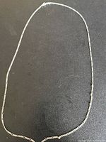 Full length photo of the silver chain laid flat on a black surface to show entire shape and length.