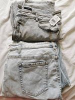 Two pairs of folded women's jeans, light blue-grey and grey with distressed knees, shown on a white surface.