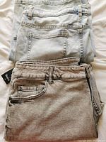 Two pairs of folded plus size jeans, one light gray and one dark gray.