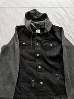 Front view of the black denim hybrid hoodie jacket showing button closure, chest pockets, distressing, grey sleeves and hood.