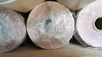 Top-down view of three large rolls of pink tissue paper wrapped in plastic, showing the smooth tightly wound edges and cylindrical cardboard core inside.