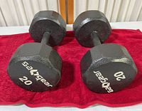 Front view of two black hexagonal 20 pound dumbbells placed on a red cloth.