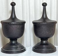 Front view of two matching bronze and metal finial bookends showing urn-shaped tops and rounded finials, dark patina finish.