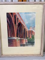 Watercolor print of an arched bridge over water, mounted in light wood frame with cream-colored matting.