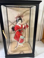 Full view of the vintage Japanese Kabuki female doll inside a black-framed glass display case, showing the doll in a red kimono with detailed fabric work and the case dimensions.