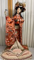 Full view of the vintage tall Kabuki female doll in orange kimono standing on fabric-covered base