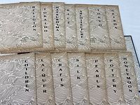 Photo showing all 14 individual pamphlets arranged on a flat surface, displaying their distinctive beige covers with swirling wave patterns and black vertical titles.