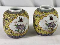 Pair of small Chinese famille rose porcelain jars shown side by side with detailed floral and bird motifs on yellow scroll background