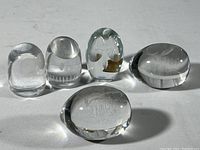 Five clear crystal pieces arranged standing and lying down including two eggs, two owls, and one character figure with face etching viewed from the side