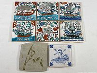 Seven ceramic tiles displayed flat, including six Greek hand painted tiles with sailing ships, one Dutch blue and white windmill tile, and one modern bamboo tile.