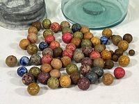 Collection of vintage clay marbles arranged on a surface near the jar, showing various colors and sizes.