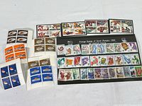 Overview of all Olympic stamps in collection, arranged on a flat surface showing variety from the three years, including unopened sealed sleeve for 1988 stamps.