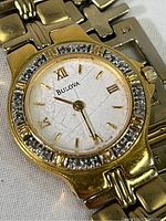 Close-up of watch face showing Bulova logo, gold-tone Roman numerals and hands, clear crystals around bezel, scratches on face surface.