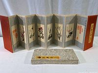 Full view of the eight-panel folding art piece displayed alongside the silk-covered presentation box, showing the accordion style and silk covers.