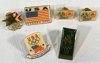 Six vintage Olympic pins shown together against white background, featuring Sydney 2000, Atlanta 1996, Special Olympics, and USA Olympic designs.