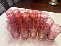 Photo showing twenty cranberry crystal drinking glasses arranged in rows, displaying the etched starburst cut design and their size.