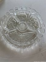 Top-down image of a round glass vegetable platter divided into four compartments with embossed vegetable and fish designs.