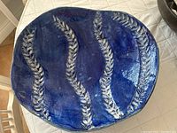 Photo of a hand-formed ceramic serving bowl with cobalt blue glaze and textured vertical leaf patterns seen on a light quilted surface.