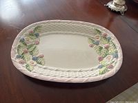 The hand painted oval ceramic platter with textured rim and colorful floral motifs laid flat on a wooden surface.