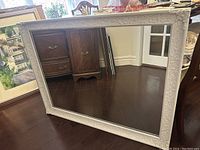 Full view of the rectangular white frame mirror showing overall condition and size on the floor reflecting furniture and room.