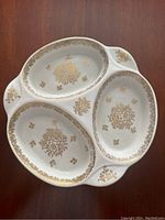 Top-down view showing three oval compartments with gold floral patterns inside each section, white porcelain background.