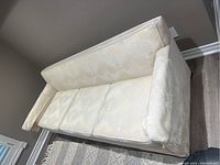 Photo showing the off-white upholstered 3-seater sofa from an angled top view, highlighting cushion and fabric texture.