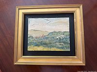 Photo of original oil painting in gilt wooden frame on a wood surface.