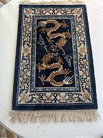 Full view of rectangular silk rug showing navy blue central field with gold dragon, cream border and fringe