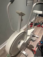 Side view of white Tunturi upright exercise bike showing flywheel, pedals, adjustable seat and handlebars.