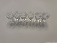 Photo showing six vintage crystal liqueur glasses arranged in a row, highlighting the art deco linear etching on each glass bowl.