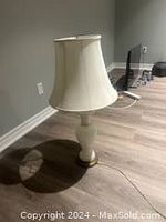 Photo of a vintage white glass lamp with an art deco style base and cream fabric lampshade on wooden floor