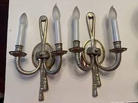 Pair of silver-tone metal wall sconces with twisted rope arms and knot motif, each holding two candle-shaped bulbs.