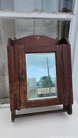 Front view of the antique wooden medicine cabinet with mirrored door closed, showing surface wear.