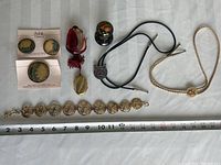 Full overhead view of the entire jewelry lot laid on white cloth, ruler included for scale.