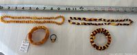 Four pieces of butterscotch amber jewelry displayed including two necklaces, a bracelet, and a ring with measuring tape for scale.
