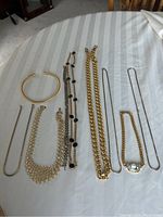 Seven pieces of costume jewelry laid out on a light striped fabric showing the entire lot.