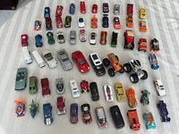 Top-down view of the collection showing multiple rows of various toy cars and trucks lined up on a white surface, displaying their colors and body types.